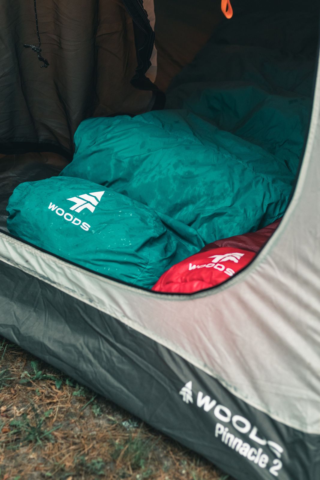 Teal and red sleeping bags with raindrops resting inside a tent doorway